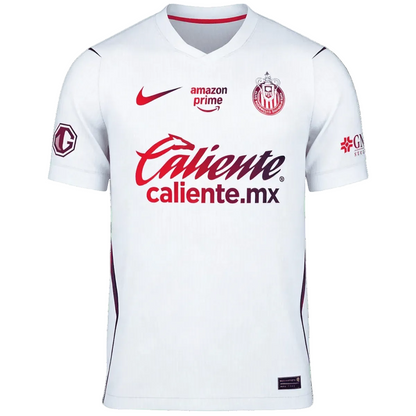 A white short-sleeve soccer jersey with red and maroon accents, Amazon Prime logo, Chivas crest, and Caliente sponsor logo on the front.