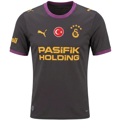 A dark gray Galatasaray soccer jersey with purple collar and sleeve trim, featuring yellow and red logos including the Turkish flag and 'PASIFIK HOLDING' sponsor text.