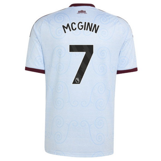 Back view of a light blue Manchester United football jersey with 'MCGINN' and the number '7' printed in black, featuring a subtle swirl pattern and maroon sleeve trim.